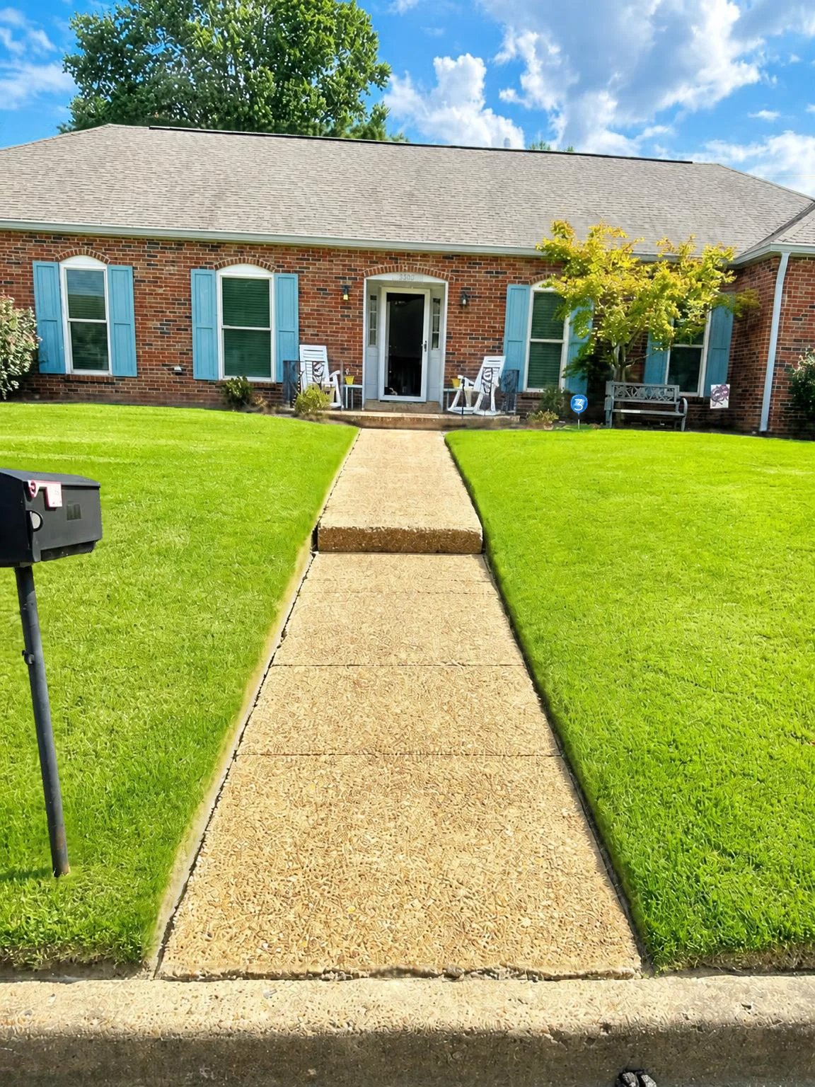 Front of the venue, a brick home with blue shutters, a green lawn, and a walkway leading to the front porch